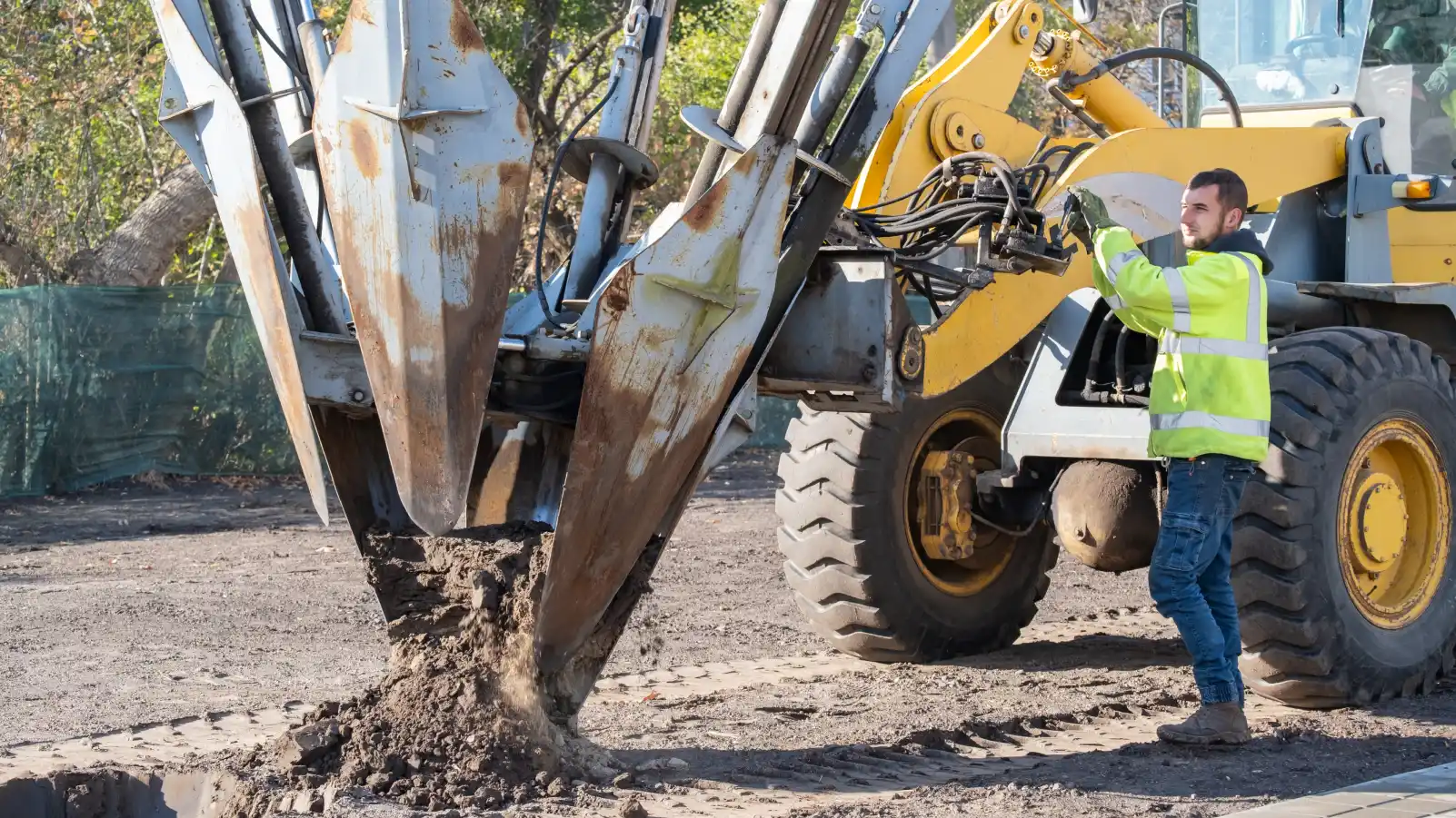 Male worker operates tree transplanter heavy machine. Landscaping, seasonal agricultural engineering, large trees landing machines. Planting of tree using tree spade - specialized machine